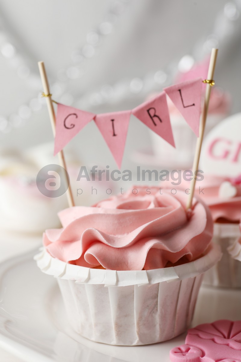 Photo of Delicious cupcake with pink cream and Girl topper for baby shower on plate, closeup