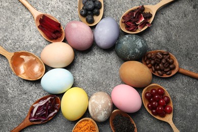 Photo of Naturally painted Easter eggs on grey table, flat lay. Turmeric, cranberries, red cabbage, onion, beetroot, blueberries, hibiscus, coffee beans and tea used for coloring