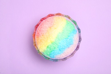 Rainbow shaving ice in glass dessert bowl on lilac background, top view