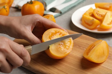 Woman cutting fresh ripe yellow tomato at light grey table, closeup