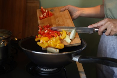Woman putting cut vegetables into frying pan in kitchen, closeup