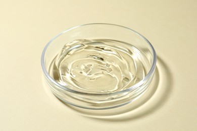 Photo of Petri dish with liquid on beige background, closeup