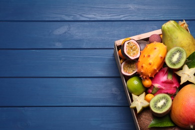 Crate with different exotic fruits on blue wooden table, top view. Space for text