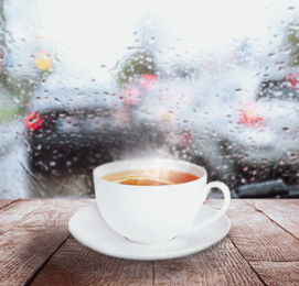 Cup of hot tea with lemon near window on rainy day 