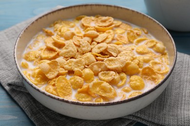Bowl of tasty corn flakes on light blue wooden table, closeup