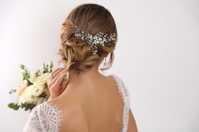 Young bride with elegant hairstyle holding wedding bouquet on white background, back view