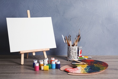 Easel with various artist tools on table against color wall. Space for text