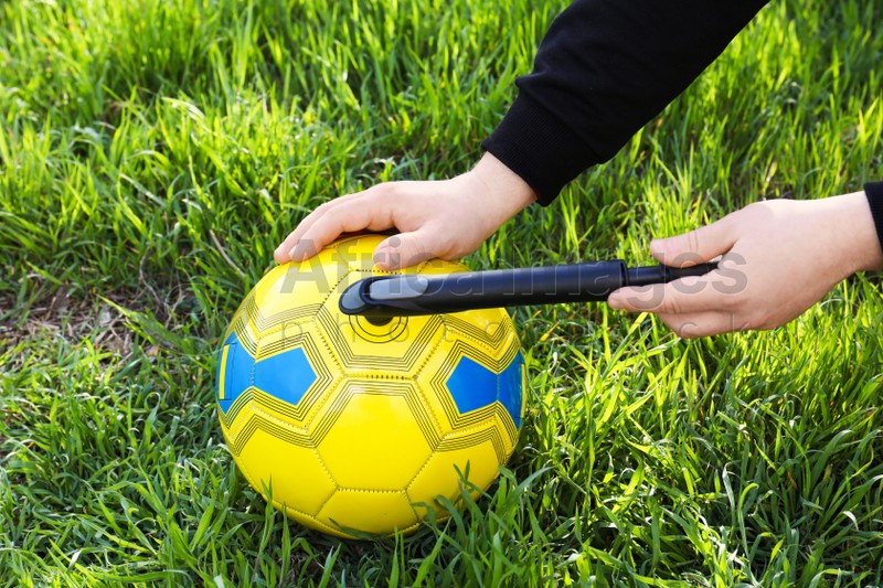 Man inflating soccer ball with manual pump on green grass, closeup