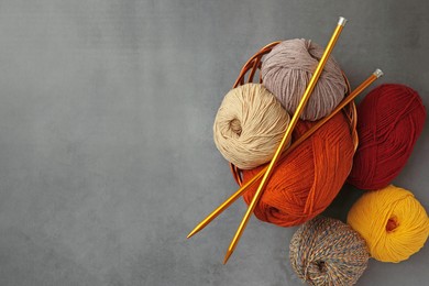 Different balls of woolen knitting yarns and needles on grey background, flat lay. Space for text