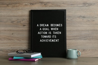 Black letter board with motivational quote a Dream Becomes a Goal When Action is Taken Toward its Achievement, notebooks and cup on wooden table