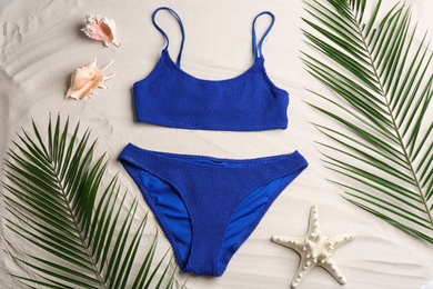 Stylish swimsuit and leaves on sand, flat lay. Beach accessory