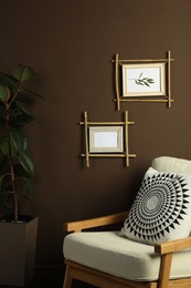 Photo of Beautiful pictures in bamboo frames on brown wall and stylish armchair indoors. Interior design