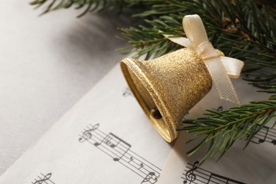 Photo of Golden shiny bell with bow, music sheets and fir branches on light table, space for text. Christmas decoration