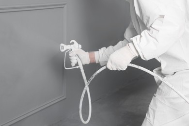 Photo of Decorator dyeing wall in grey color with spray paint, closeup