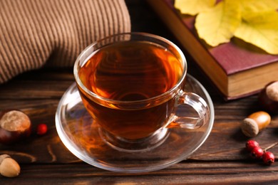 Cup of aromatic tea, book and acorns on wooden table indoors, closeup. Autumn atmosphere