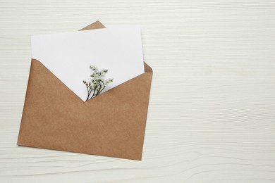 Envelope with blank paper card and flowers on white wooden table, top view. Space for text