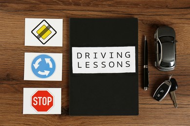 Flat lay composition with workbook for driving lessons and road signs on wooden background. Passing license exam