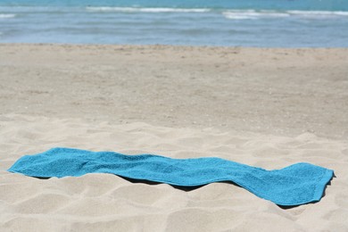 Soft blue towel on sandy beach near sea, space for text