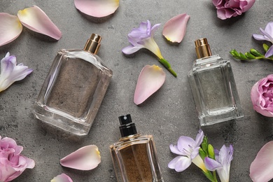 Photo of Flat lay composition of different perfume bottles, roses and freesia flowers on dark textured background