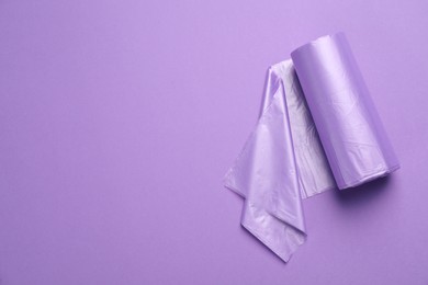 Photo of Roll of color garbage bags on violet background, top view. Space for text