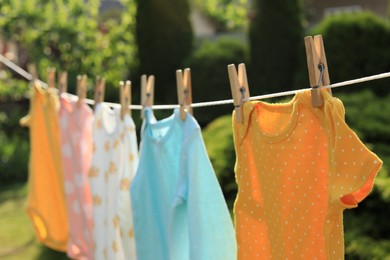 Clean baby onesies hanging on washing line in garden, closeup. Drying clothes