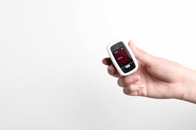 Photo of Woman holding fingertip pulse oximeter on white background, closeup. Space for text