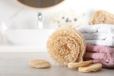 Natural loofah sponges and towels on table in bathroom, closeup. Space for text