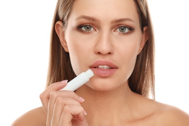 Young woman with cold sore applying lip balm against white background