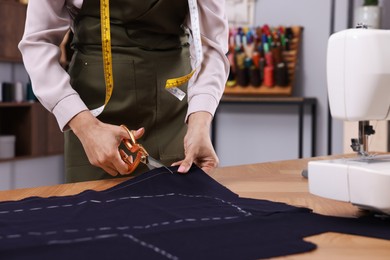 Dressmaker cutting fabric by following chalked sewing pattern in workshop, closeup