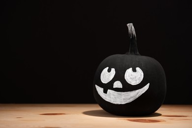 Halloween celebration. Pumpkin with drawn face on wooden table against black background, space for text