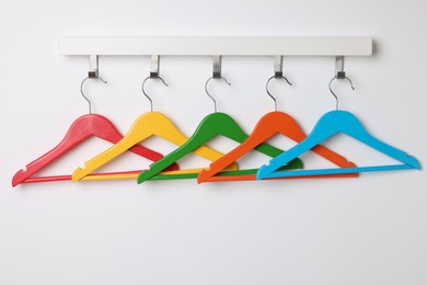 Rack with empty bright clothes hangers on white wall