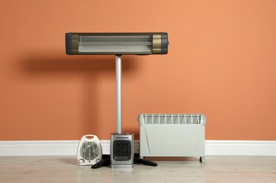 Different electric heaters near orange wall indoors