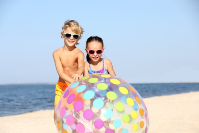 Little children with inflatable ball on sandy beach near sea. Summer holidays