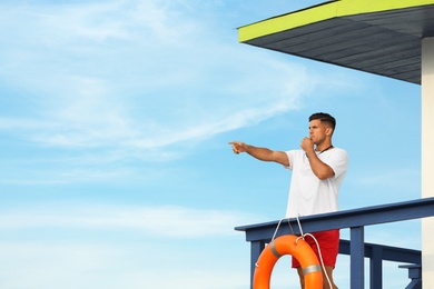 Male lifeguard with whistle on watch tower against blue sky