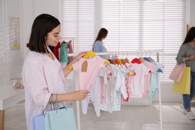 Happy pregnant woman with shopping bags choosing baby clothes in store