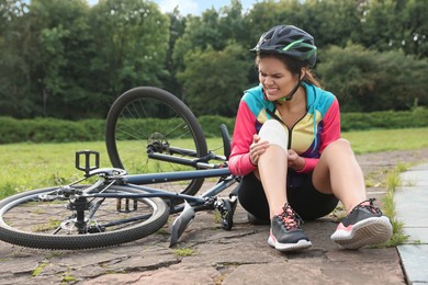 Young woman applying bandage onto her knee near bicycle outdoors
