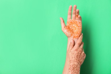 Woman with henna tattoos on hands against green background, closeup and space for text. Traditional mehndi ornament
