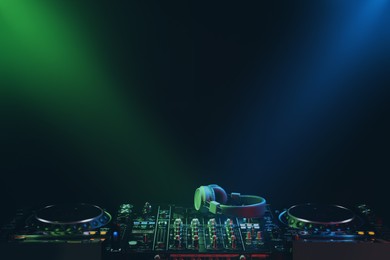 Modern DJ controller and headphones under beams of light on black background