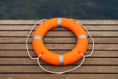 Orange lifebuoy on wooden pier near water. Rescue equipment