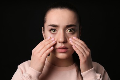 Woman checking her health condition on black background. Yellow eyes as symptom of problems with liver
