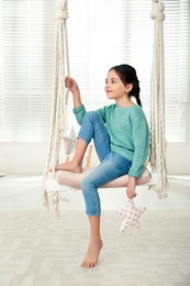 Cute little girl playing on swing at home