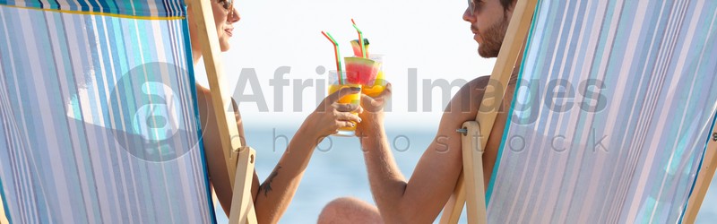 Young couple with cocktails in beach chairs at seacoast. Banner design