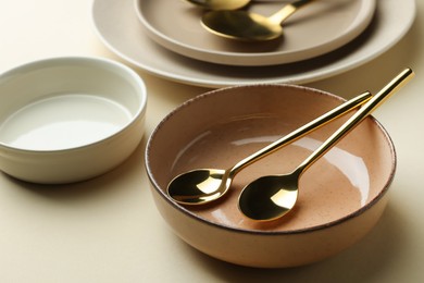 Stylish empty dishware and spoons on beige background, closeup