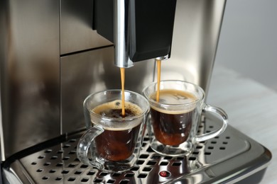 Modern espresso machine pouring coffee into glass cups on table, closeup