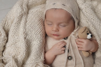 Adorable newborn baby with toy bear sleeping on knitted plaid, top view