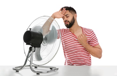 Man suffering from heat in front of fan on white background. Summer season