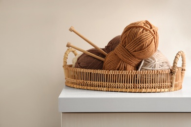 Photo of Woolen yarns and knitting needles in basket on white wooden table