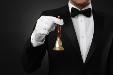 Butler holding hand bell on black background, closeup