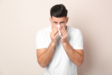 Photo of Man with tissue suffering from runny nose on beige background