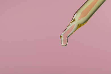 Dripping hydrophilic oil from pipette on pink background, closeup. Space for text